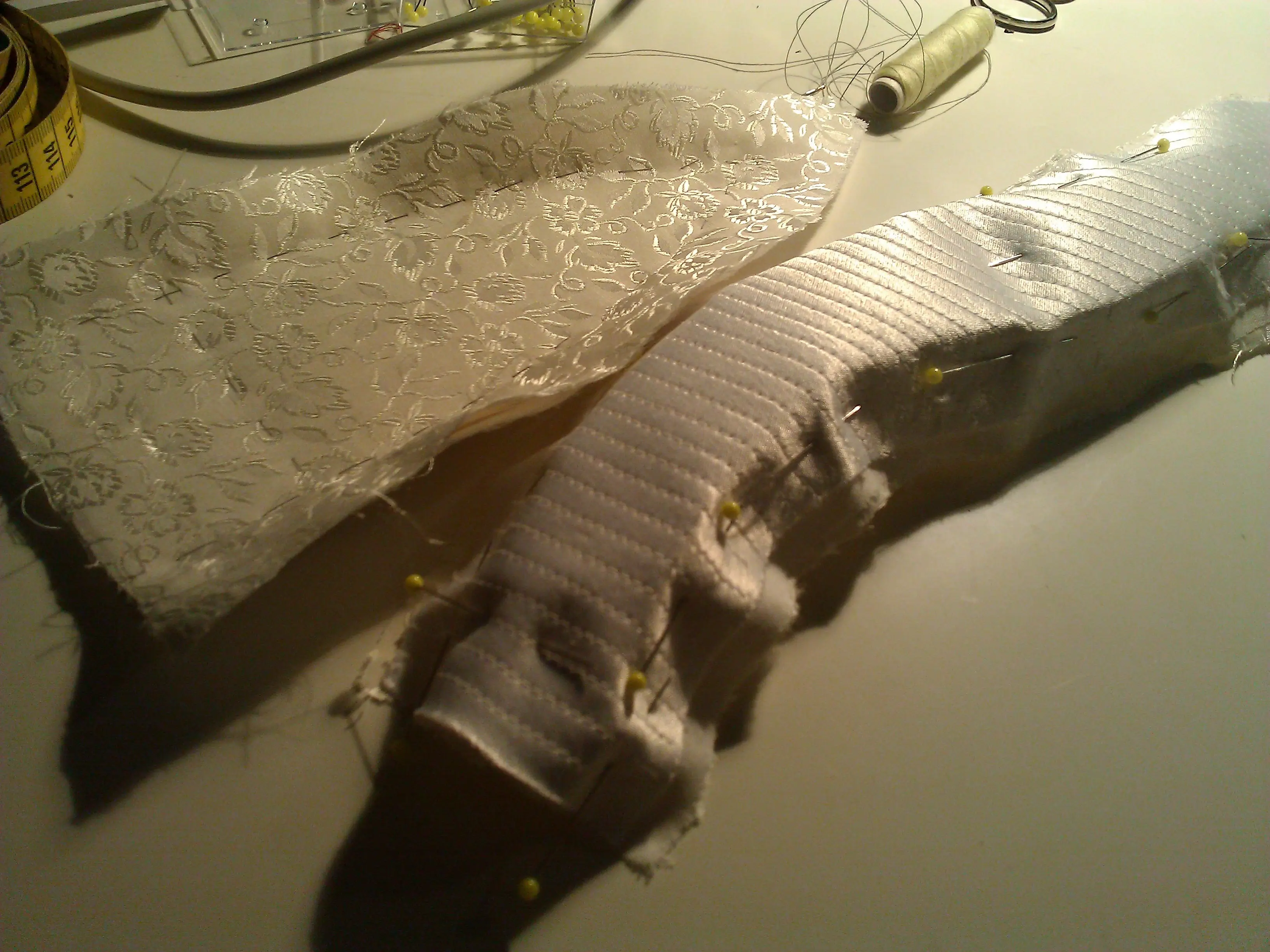 Ivory silk covering pinned onto the boned linen stays on a work table