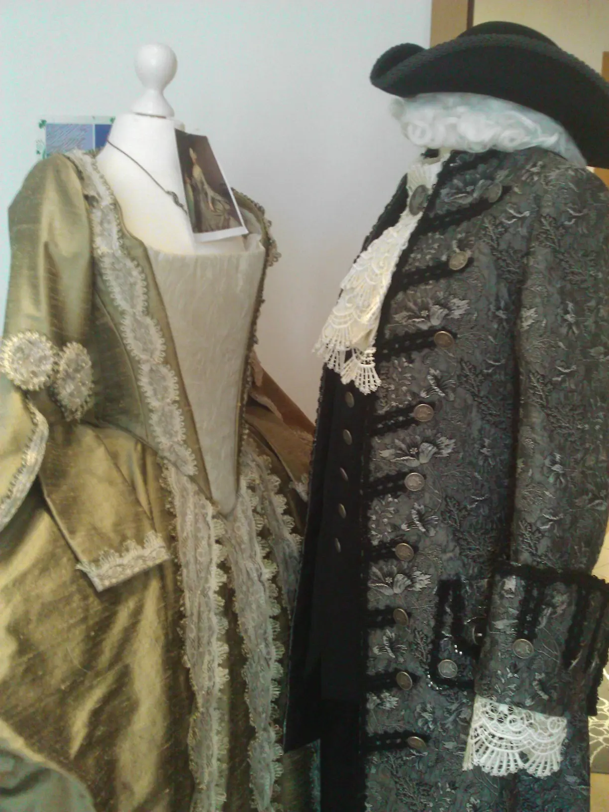 The finished gold gown and grey justaucorps with tricorn displayed together in the atelier